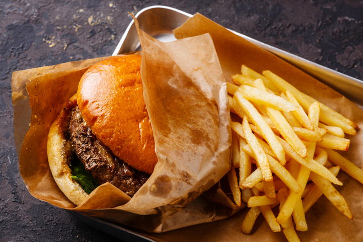 Top 10 Foods To Avoid This Winter Burger with meat and French fries in aluminum tray on dark background