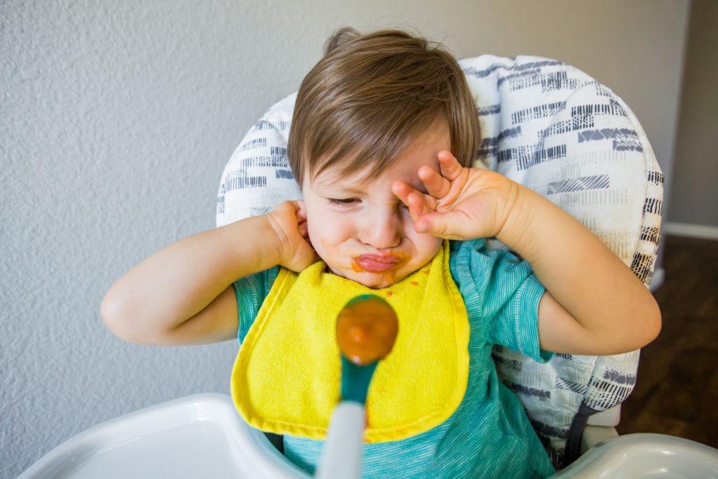Toddler being picky and fussy while being fed baby food.