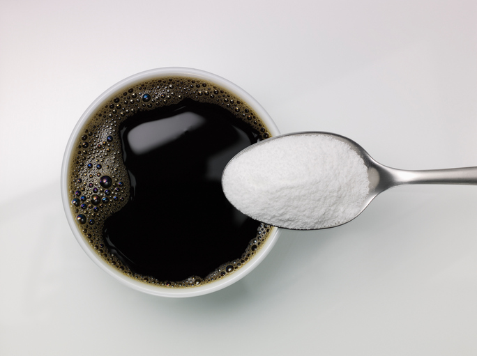 Spoon of sugar above a cup of coffee