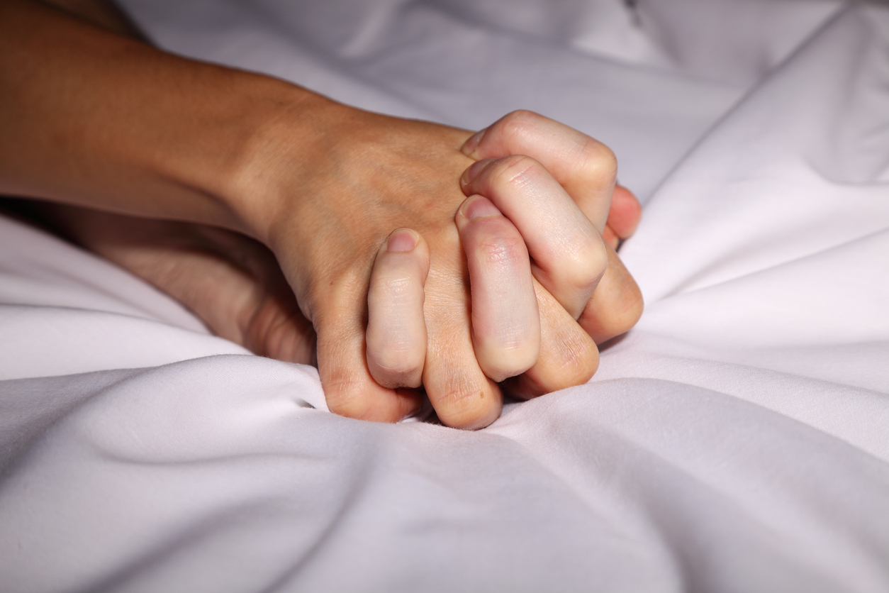 Couple in bed holding hands passionately