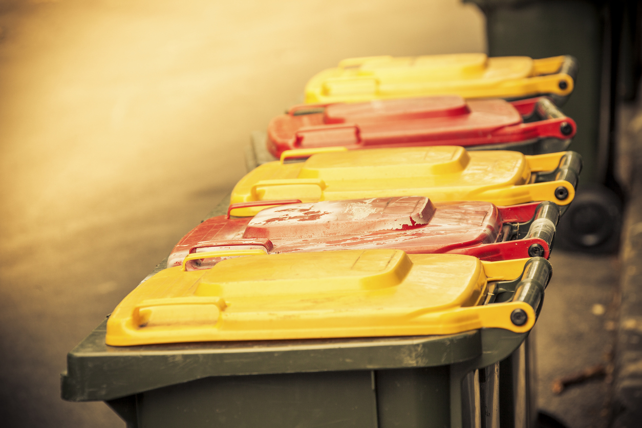 Ready for the garbos: yellow and red-topped garbage bins in alternating colours outside in a residential back alley. Closed (lids down), Selective focus (on second bin), horizontal, copy space, some noise for effect.