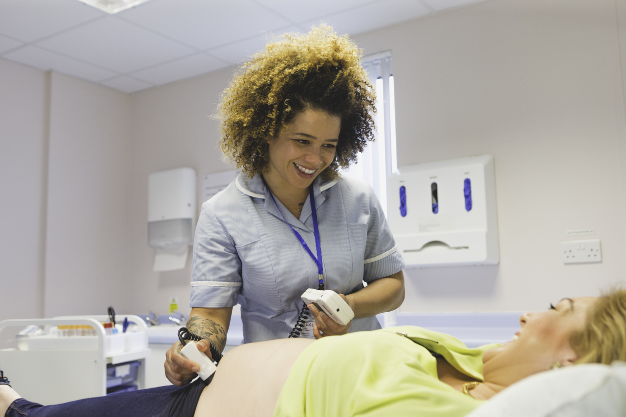 Pregnant woman having an ultrasound at doctor's office, female gynaecologist using a transducer