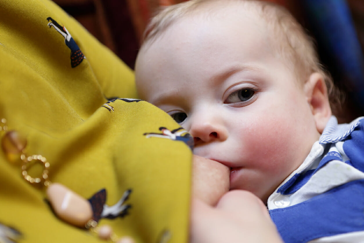 Serious baby sucks mother's breast at home